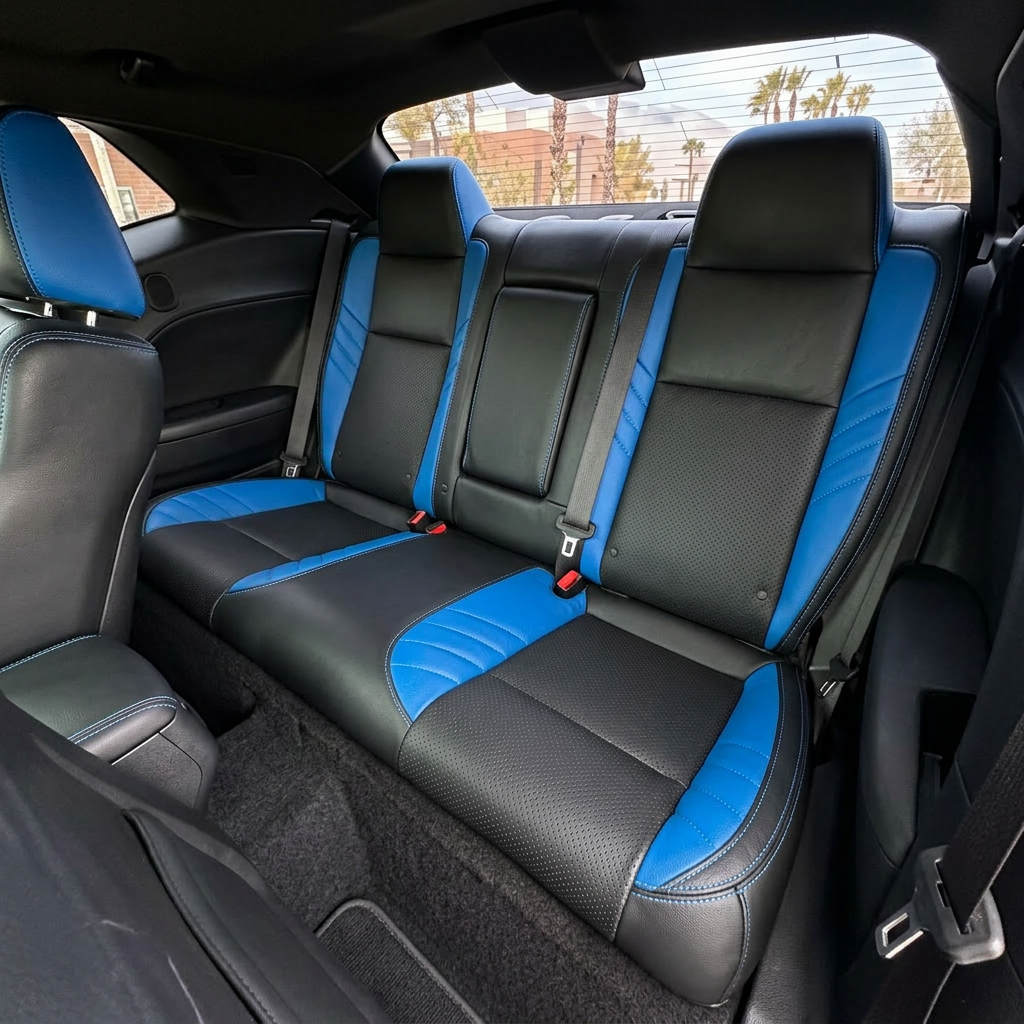 Rear in-cabin view of a 2015–2023 Dodge Challenger Hellcat with Leatherteck rear seat covers installed in black, featuring perforated combination inserts, Bermuda Blue exotic vinyl accent panels, and Bermuda Blue contrast stitching throughout, with the rear bench seat, headrests, seatbelts, front seatback, side panels, and rear window visible.